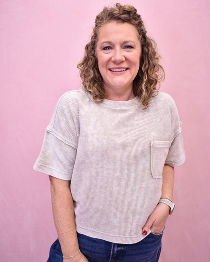 Woman wearing a light-colored t-shirt with a pocket against a pink background