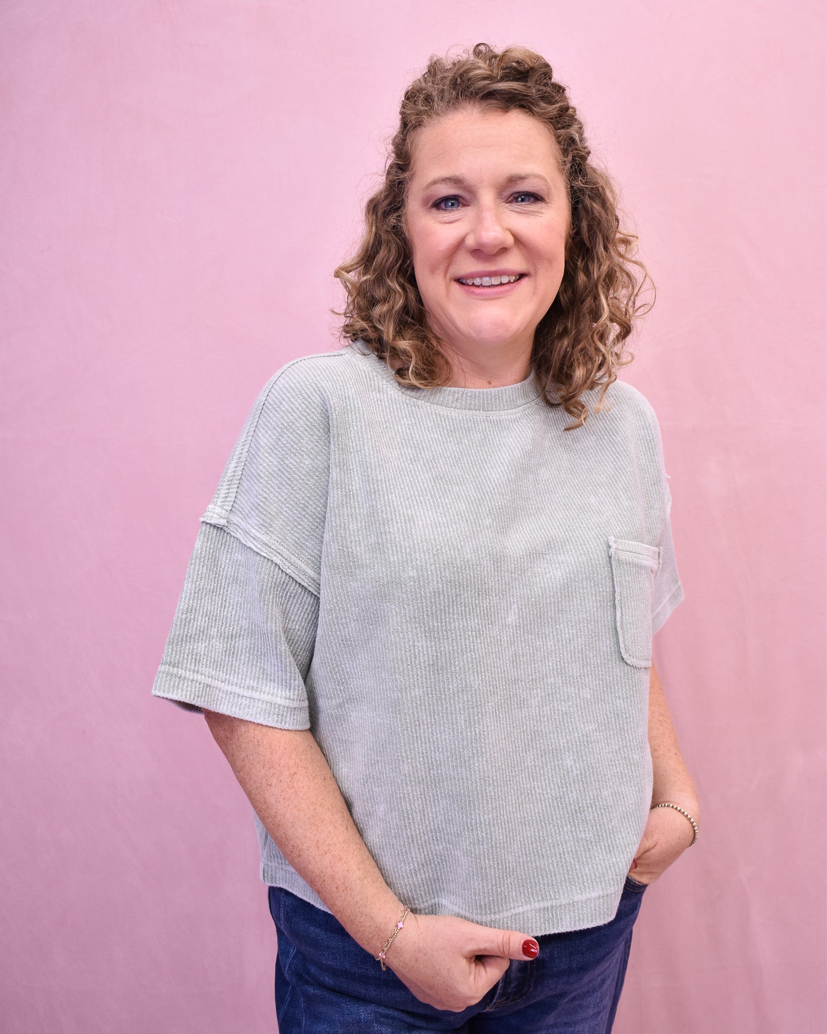 Woman wearing a light gray textured sweater against a pink background