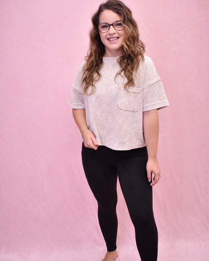 Woman wearing a light-colored t-shirt with a pocket and black leggings on a pink background