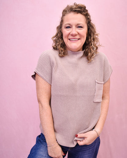 Woman wearing a light brown ribbed sweater against a pink background