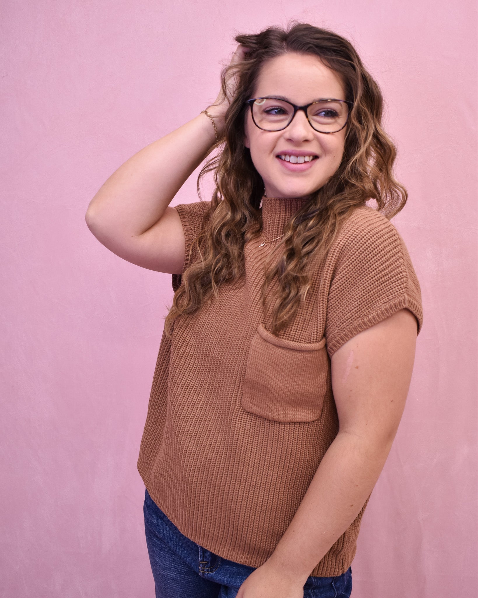 Woman wearing a brown knitted sleeveless sweater against a pink background