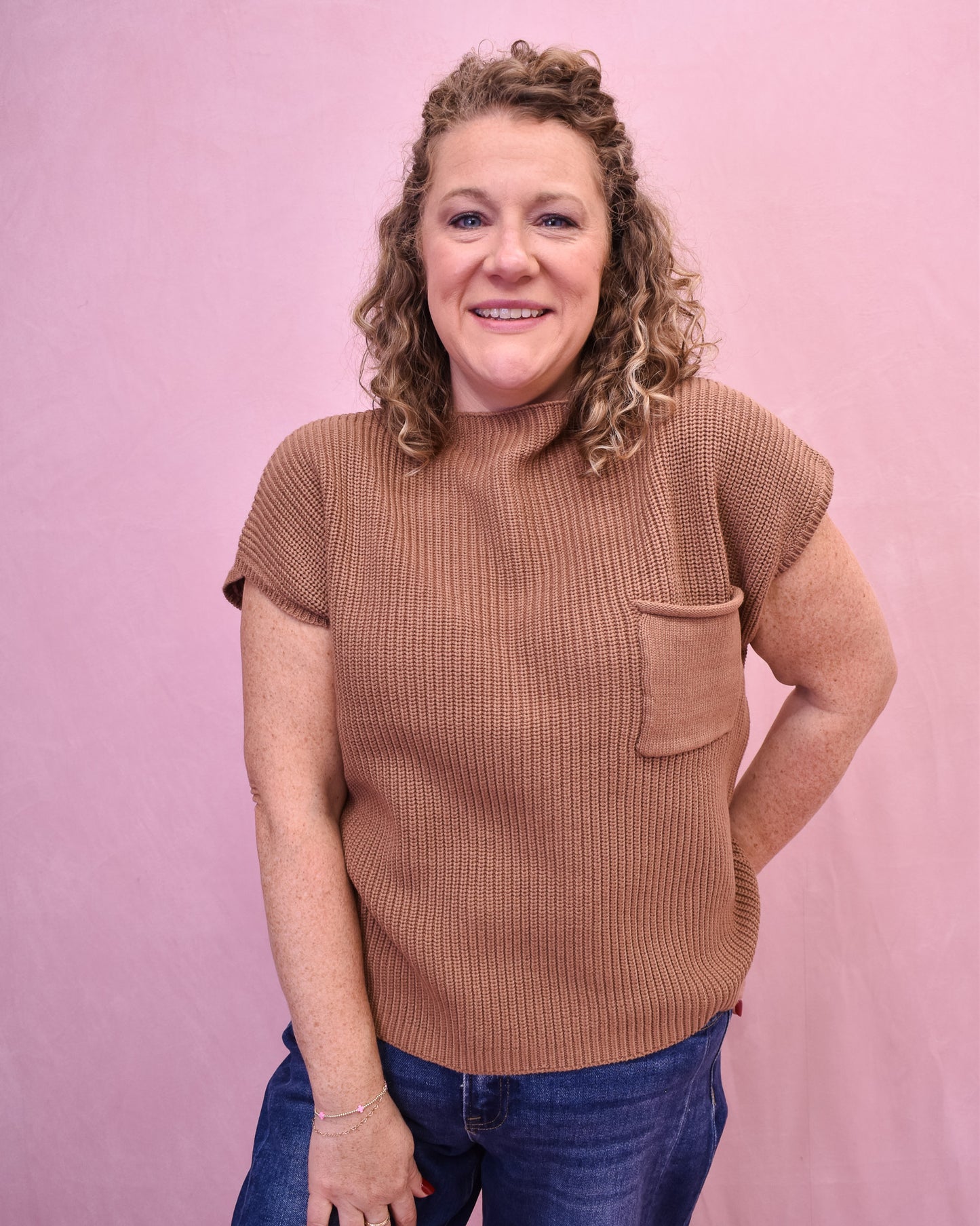 Woman wearing a brown ribbed sweater with a pocket against a pink background