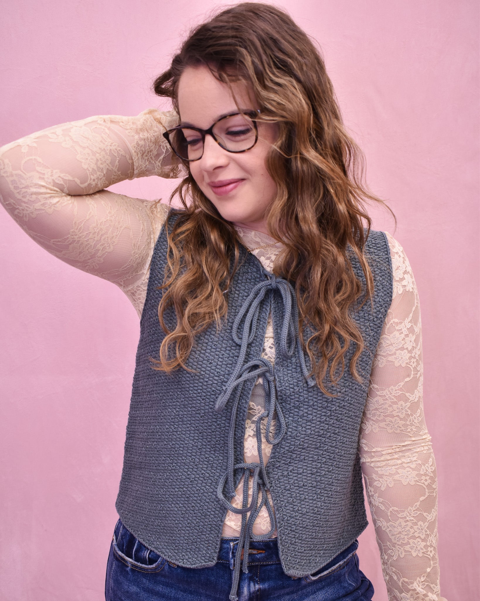 Woman wearing a blue knitted vest against a pink background