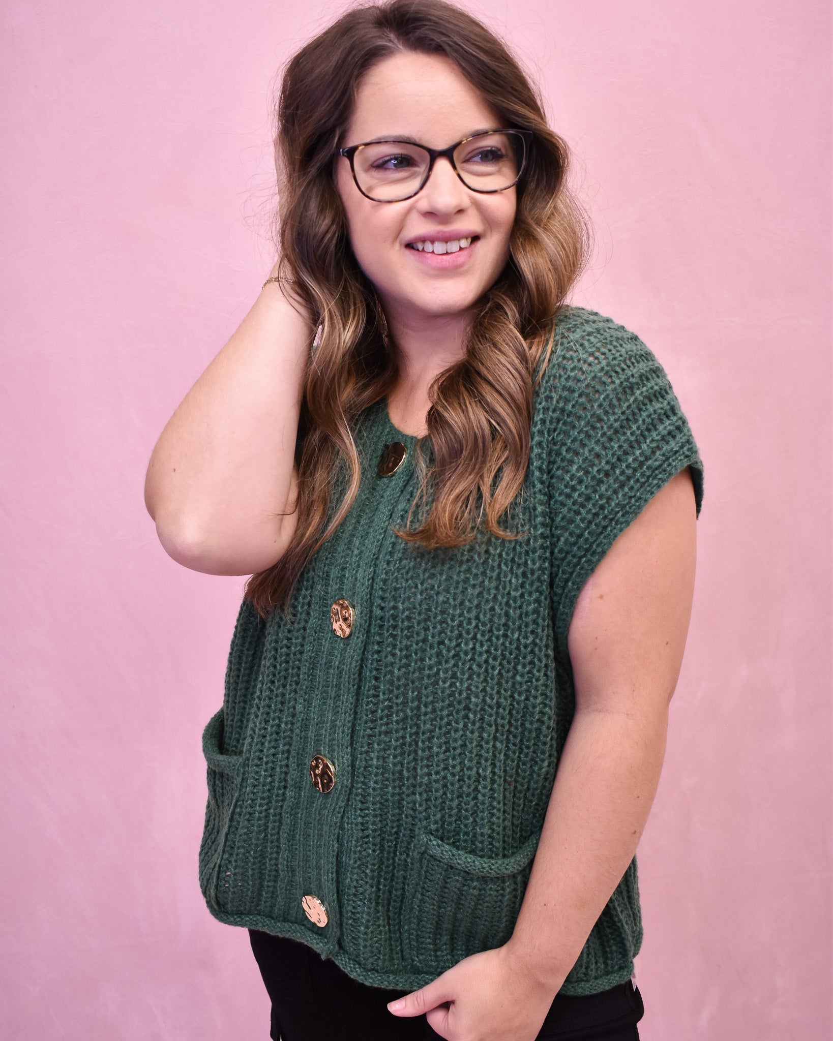 Woman wearing a green knitted vest against a pink background
