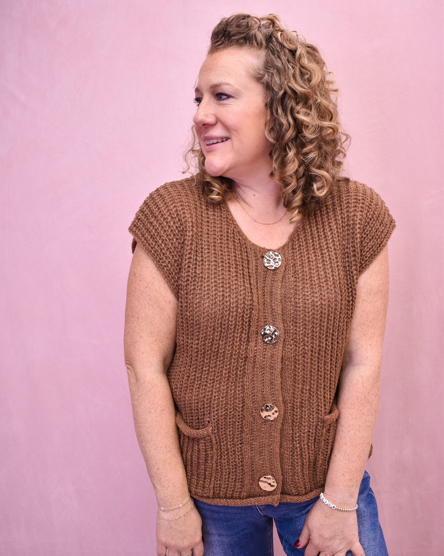 Woman wearing a brown knitted vest with buttons against a pink background