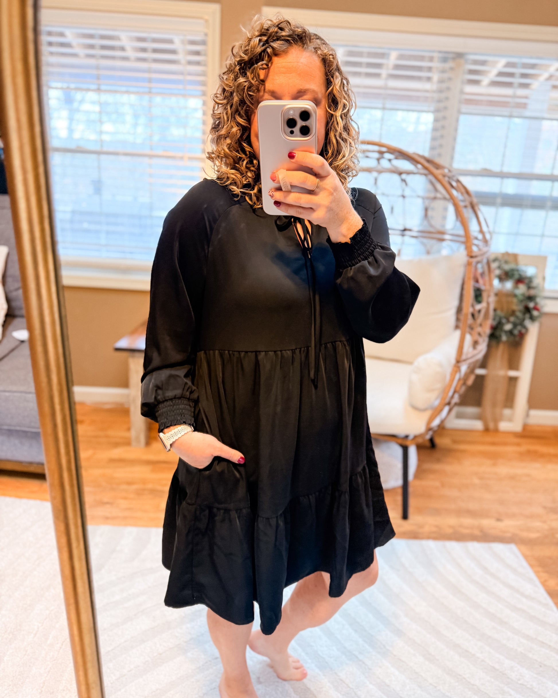 Woman taking a mirror selfie wearing a black dress in a home setting.