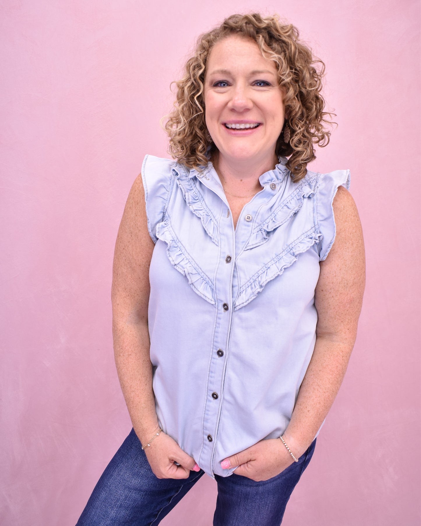 Woman wearing a light blue sleeveless shirt with ruffles on a pink background