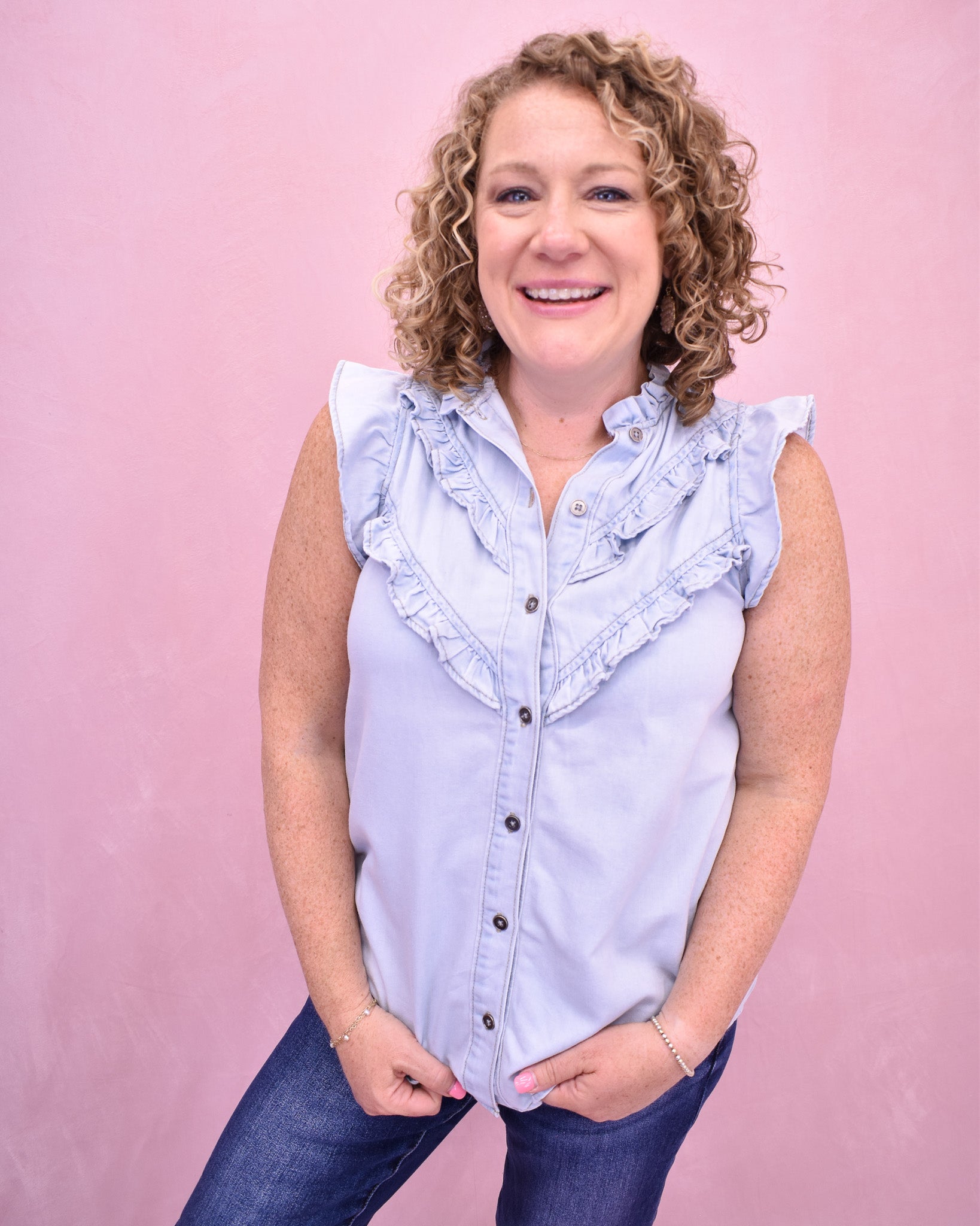 Woman wearing a light blue sleeveless shirt with ruffles on a pink background