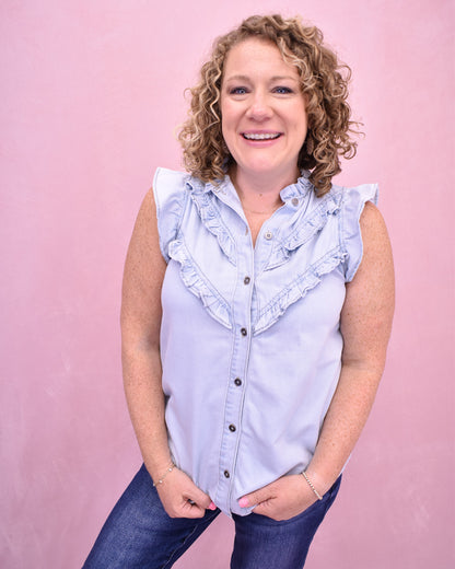 Woman wearing a light blue sleeveless shirt with ruffles on a pink background