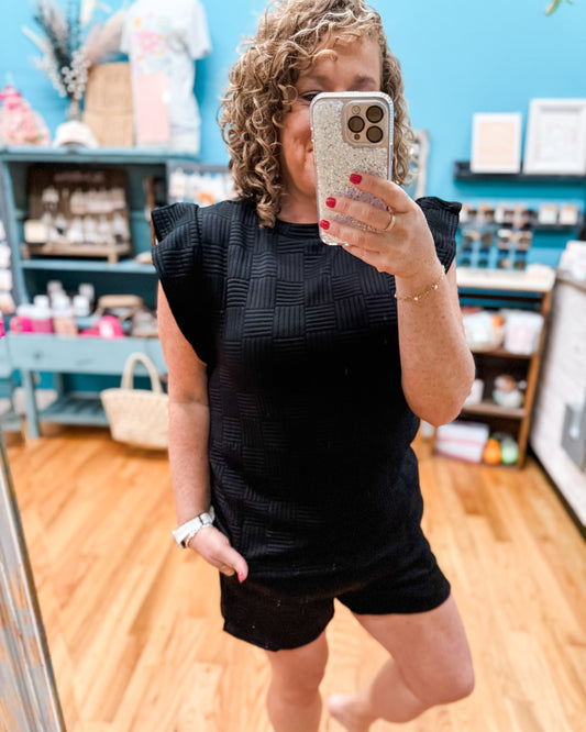 Person taking a mirror selfie wearing a black outfit in a store setting.