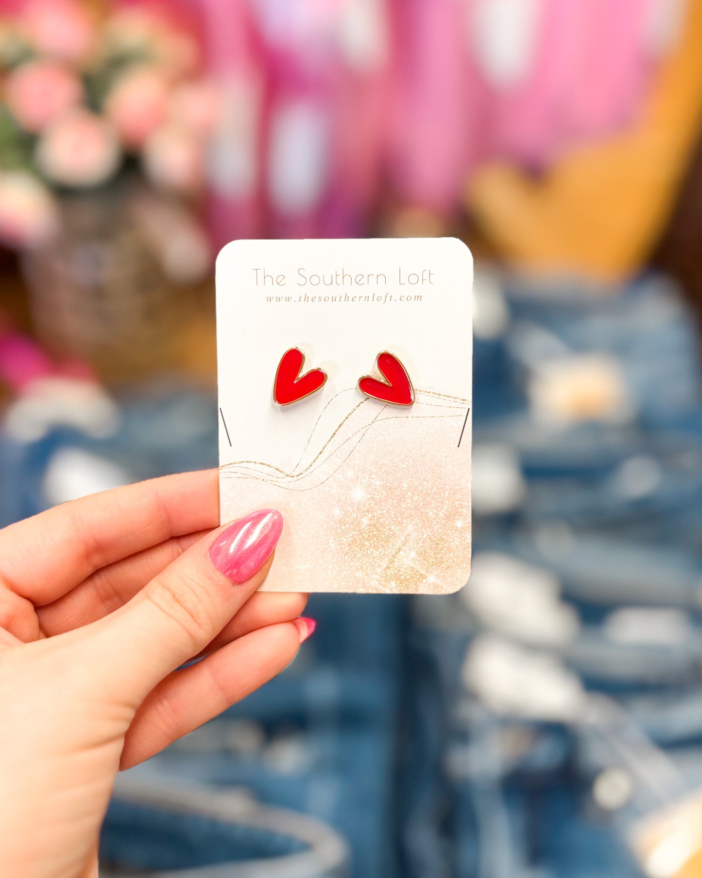 Card with red heart-shaped earrings held by a hand against a blurred background
