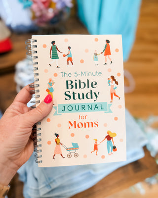 Hand holding 'The 5-Minute Bible Study Journal for Moms' with colorful illustrations on a blurred background