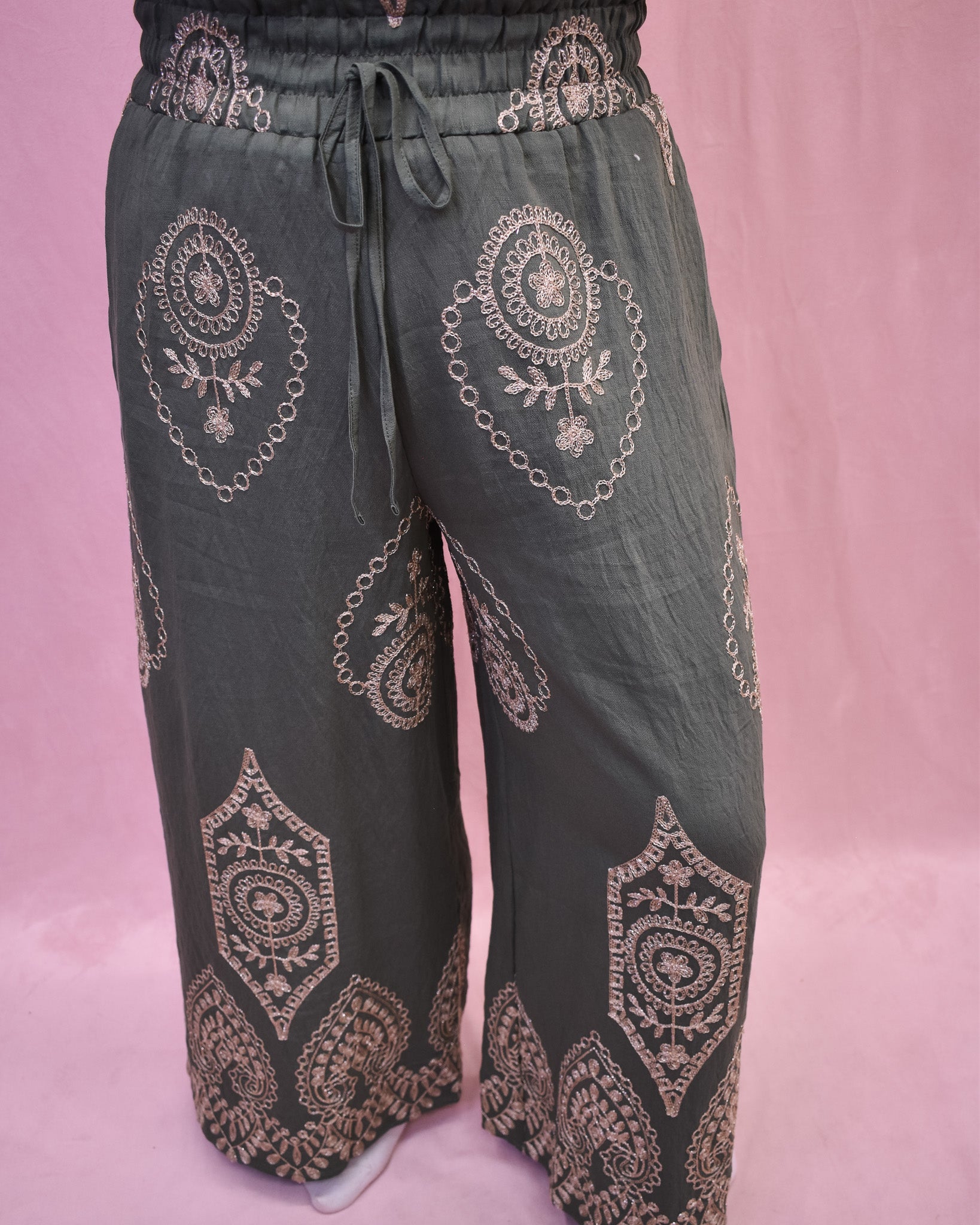 Dark green pants with intricate gold embroidery on a pink background