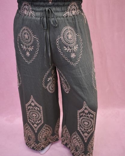 Dark green pants with intricate gold embroidery on a pink background