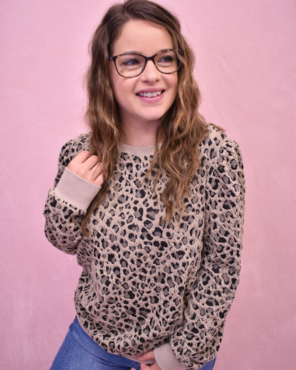 Person wearing a leopard print sweater against a pink background
