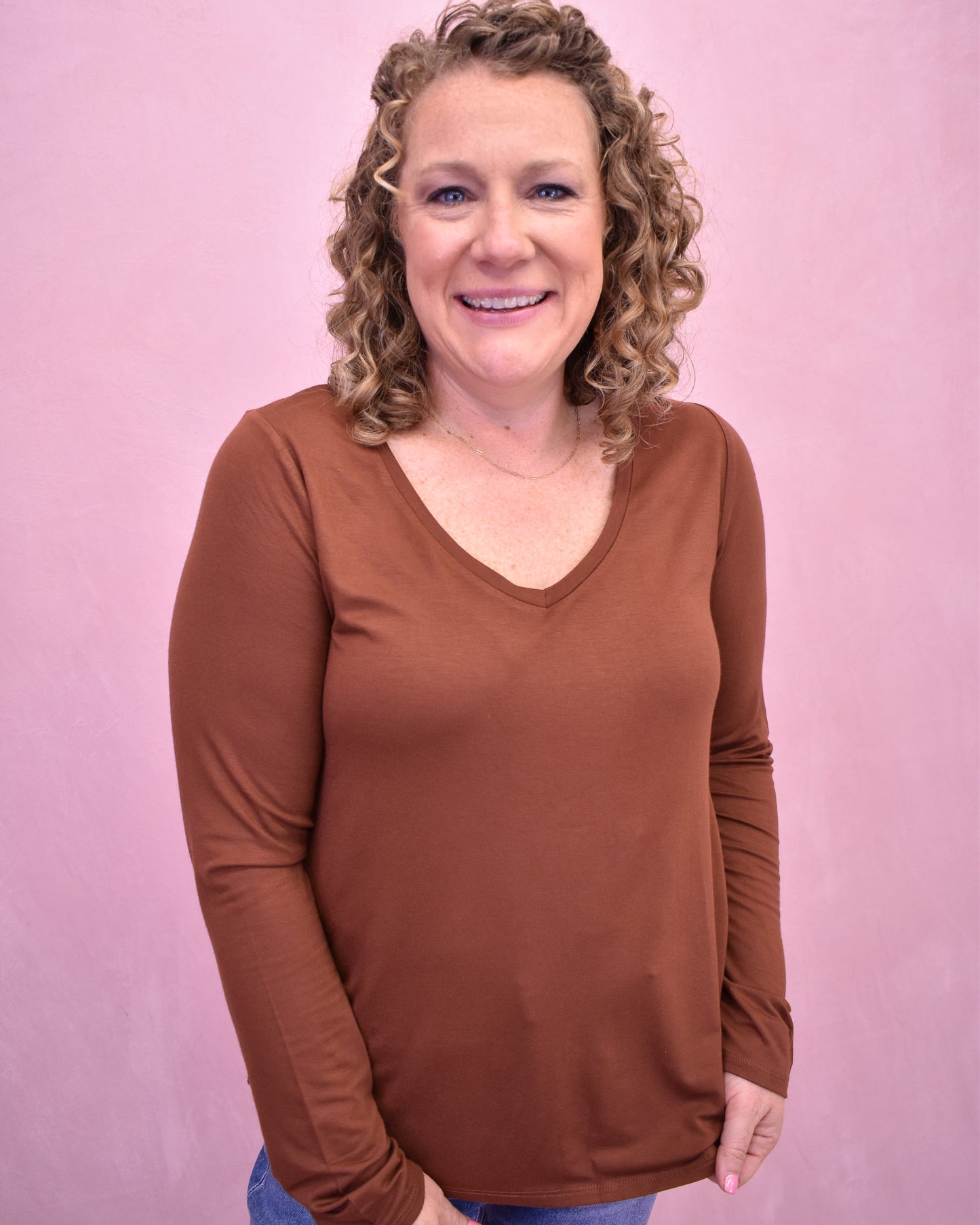 Woman wearing a brown long-sleeve top against a pink background