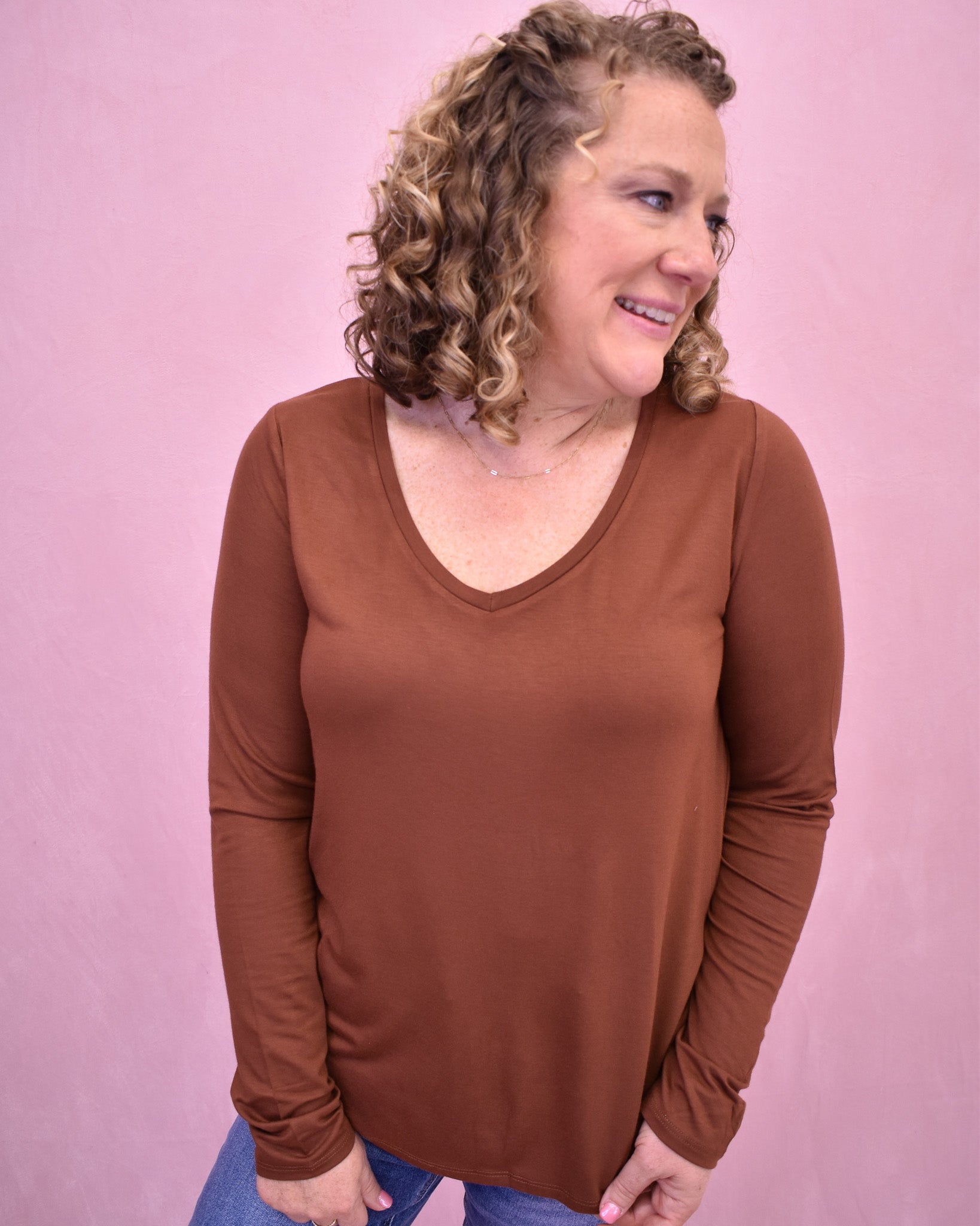 Woman wearing a brown long-sleeve top against a pink background