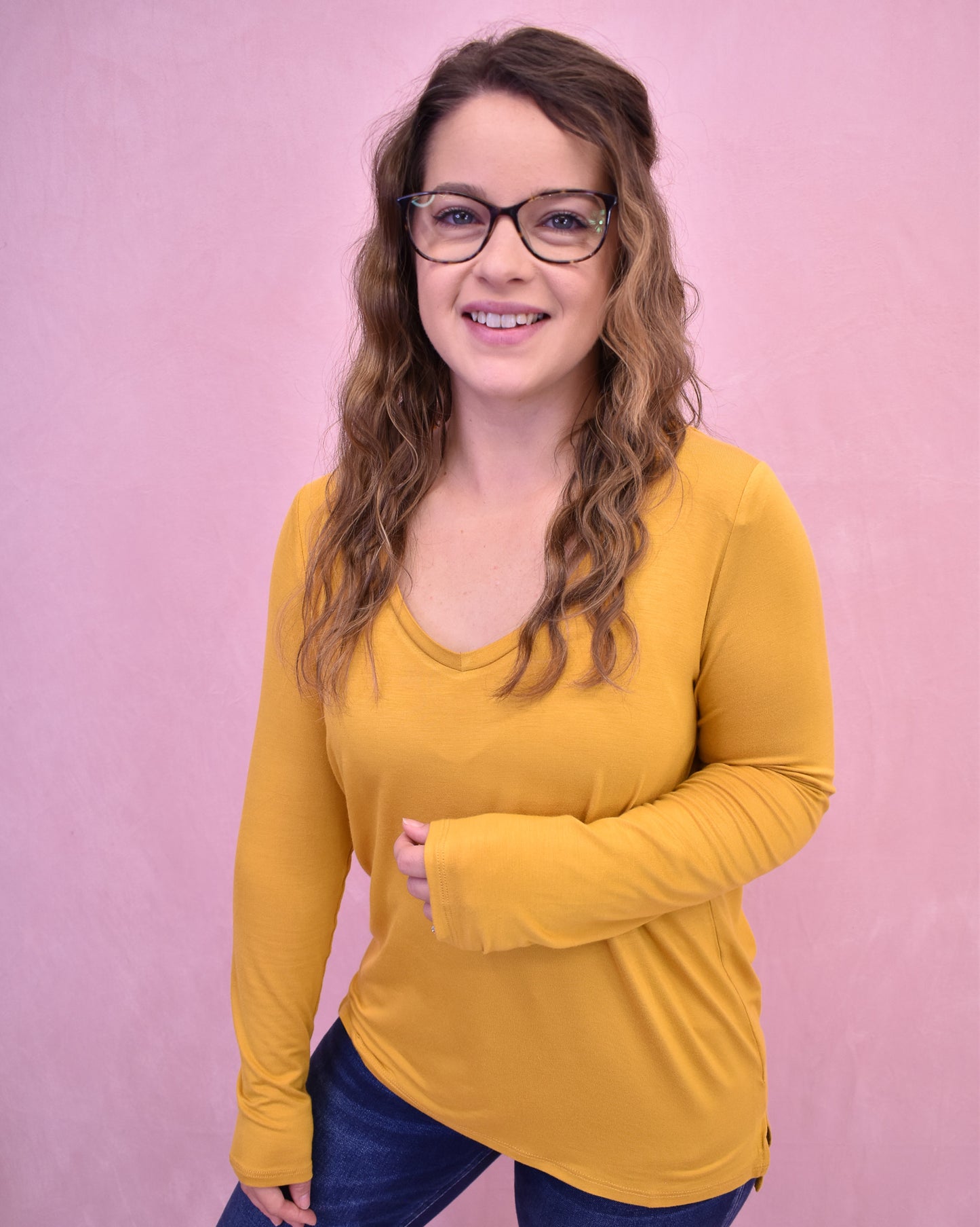 Woman wearing a yellow long-sleeve shirt against a pink background
