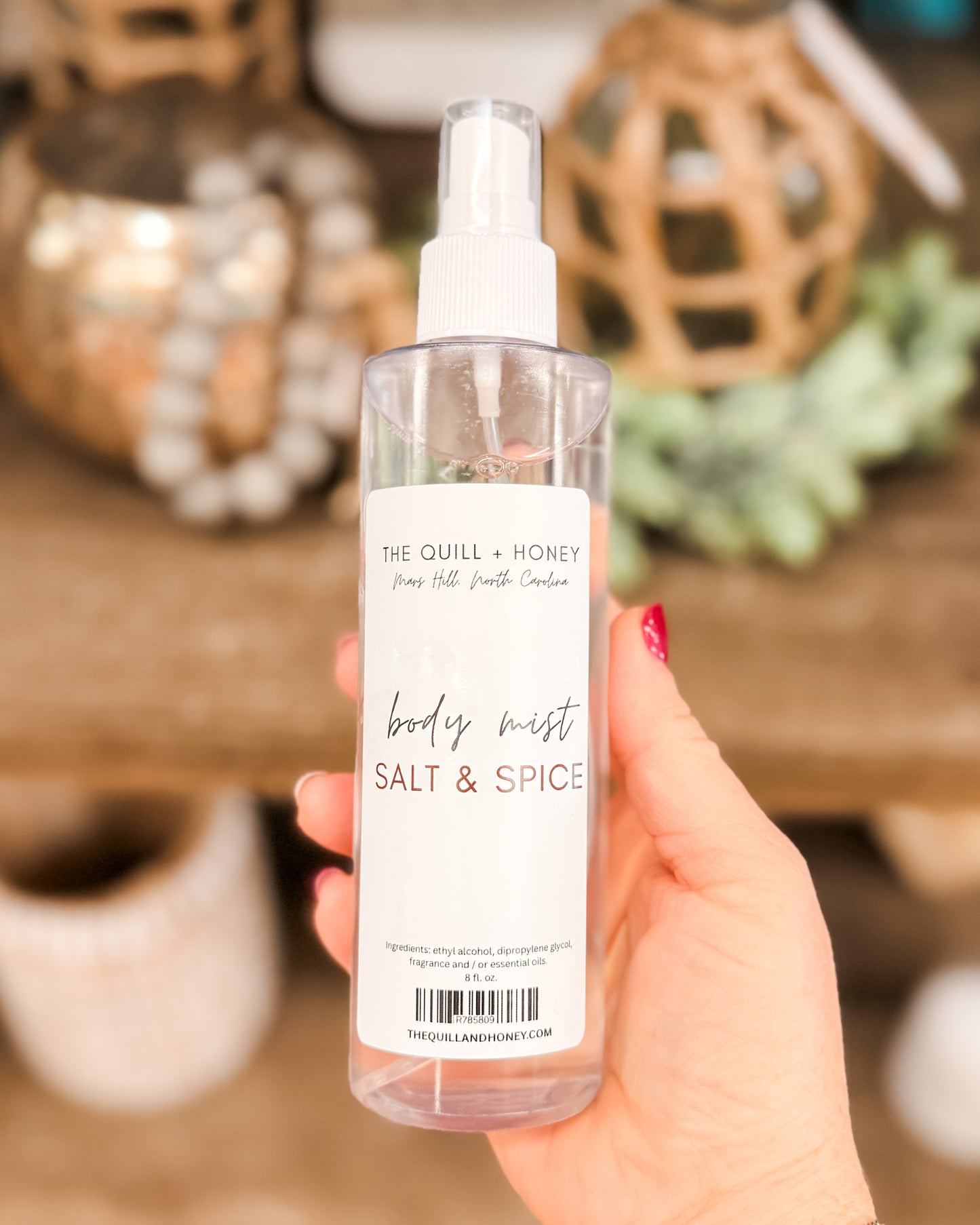Hand holding a bottle of 'Salt & Spice' body mist with decorative background