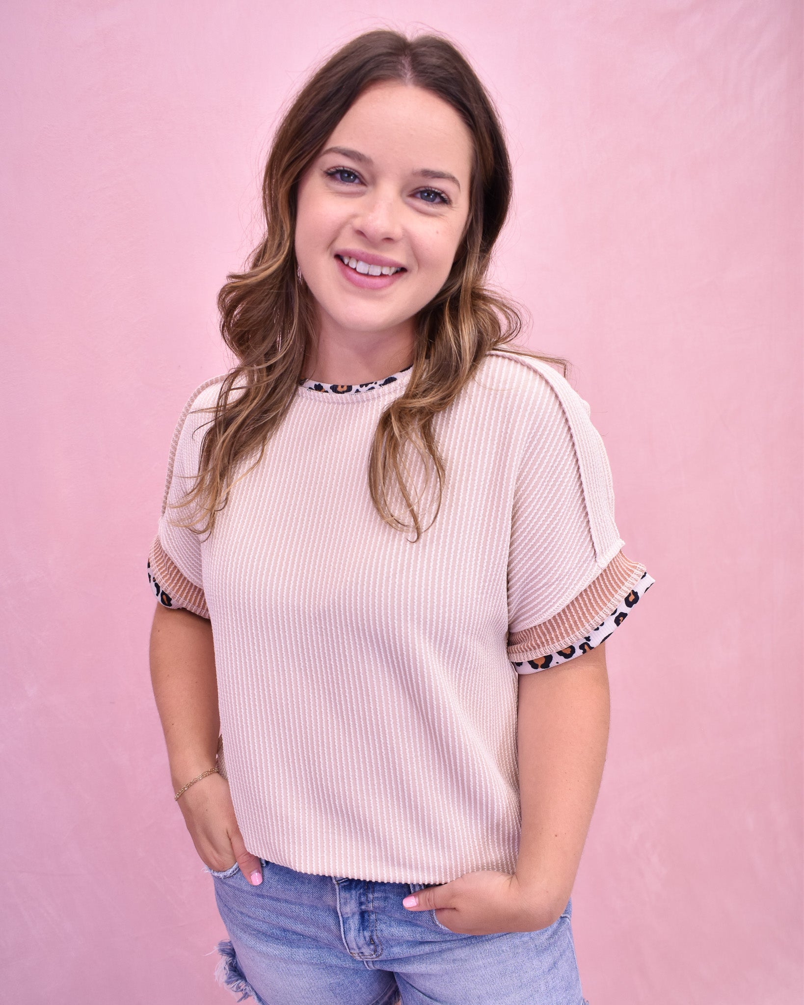 Woman wearing a light pink ribbed top with patterned sleeves against a pink background