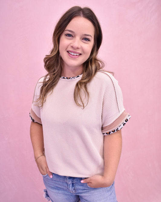 Woman wearing a light pink ribbed top with patterned sleeves against a pink background