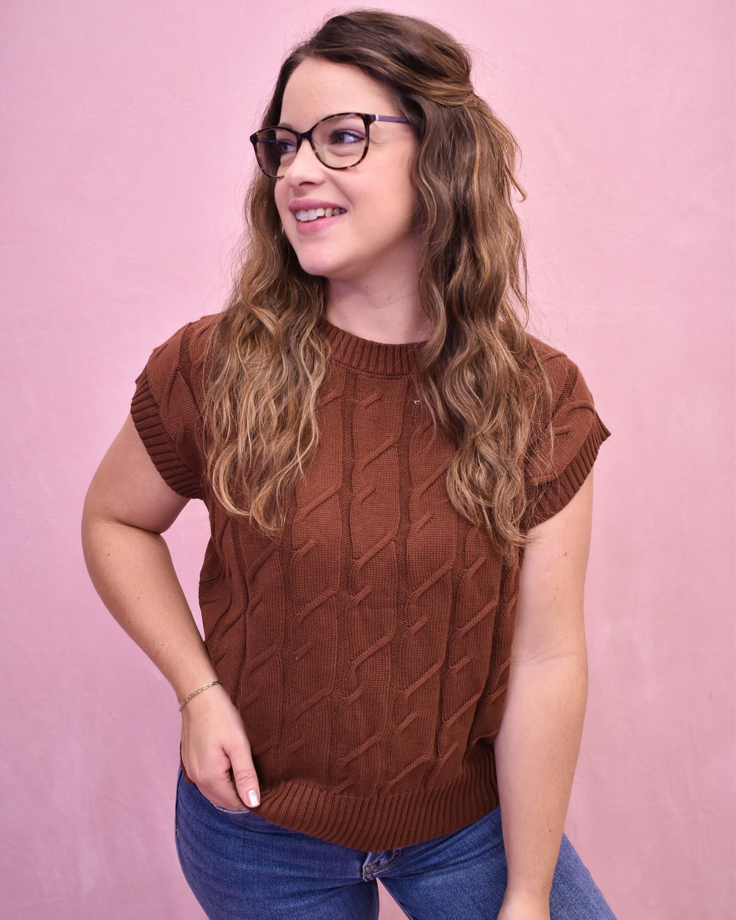 Woman wearing a brown sleeveless sweater against a pink background