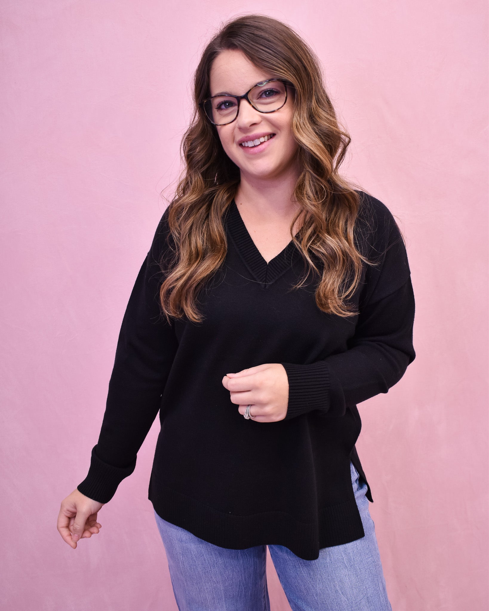 Woman wearing a black sweater and glasses against a pink background
