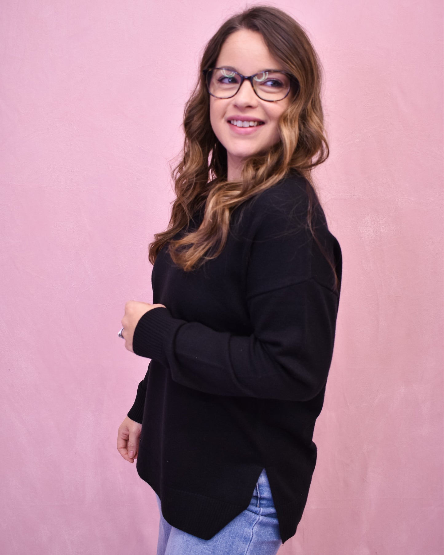 Woman wearing a black sweater and glasses against a pink background