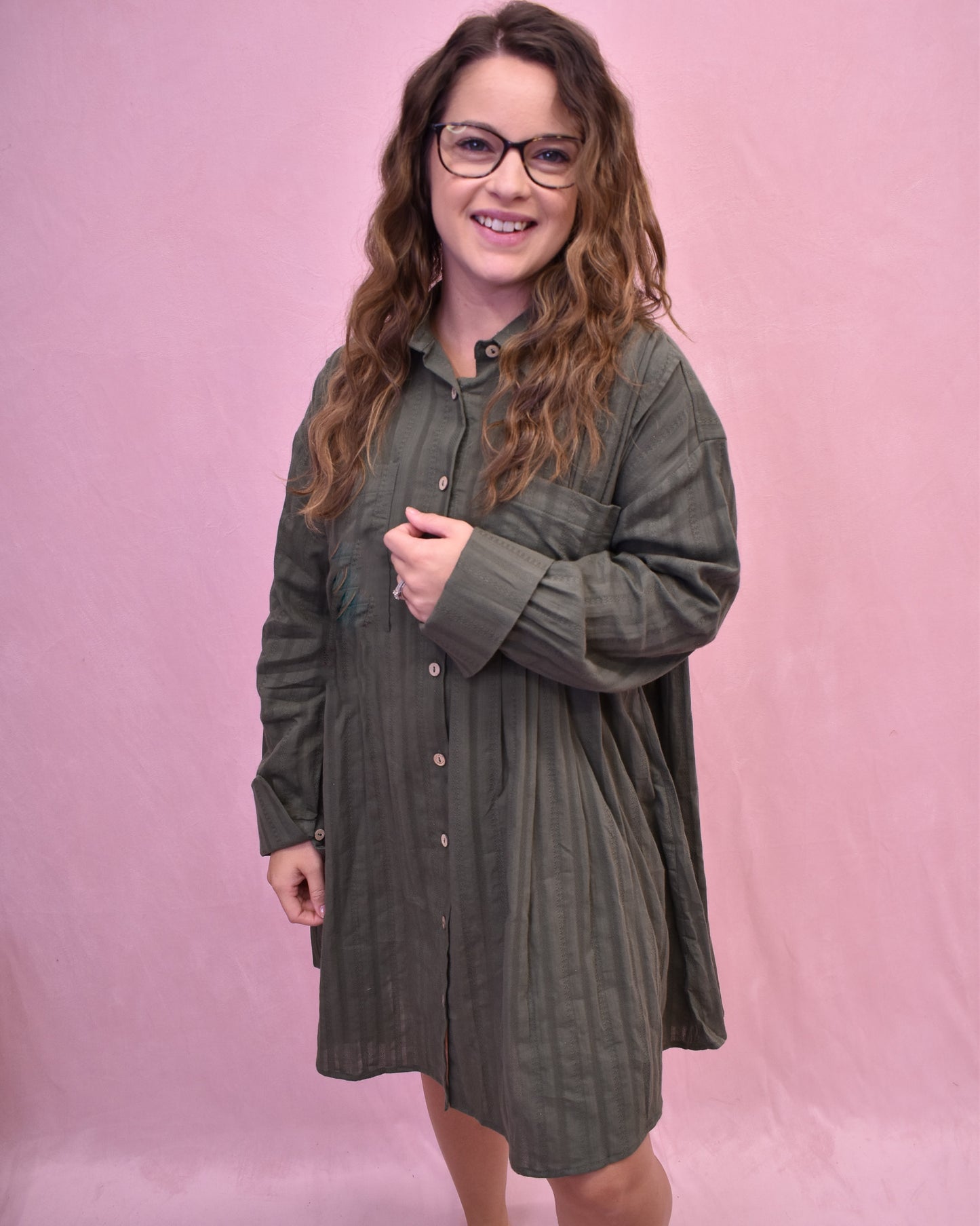 Woman wearing a green dress with long sleeves against a pink background