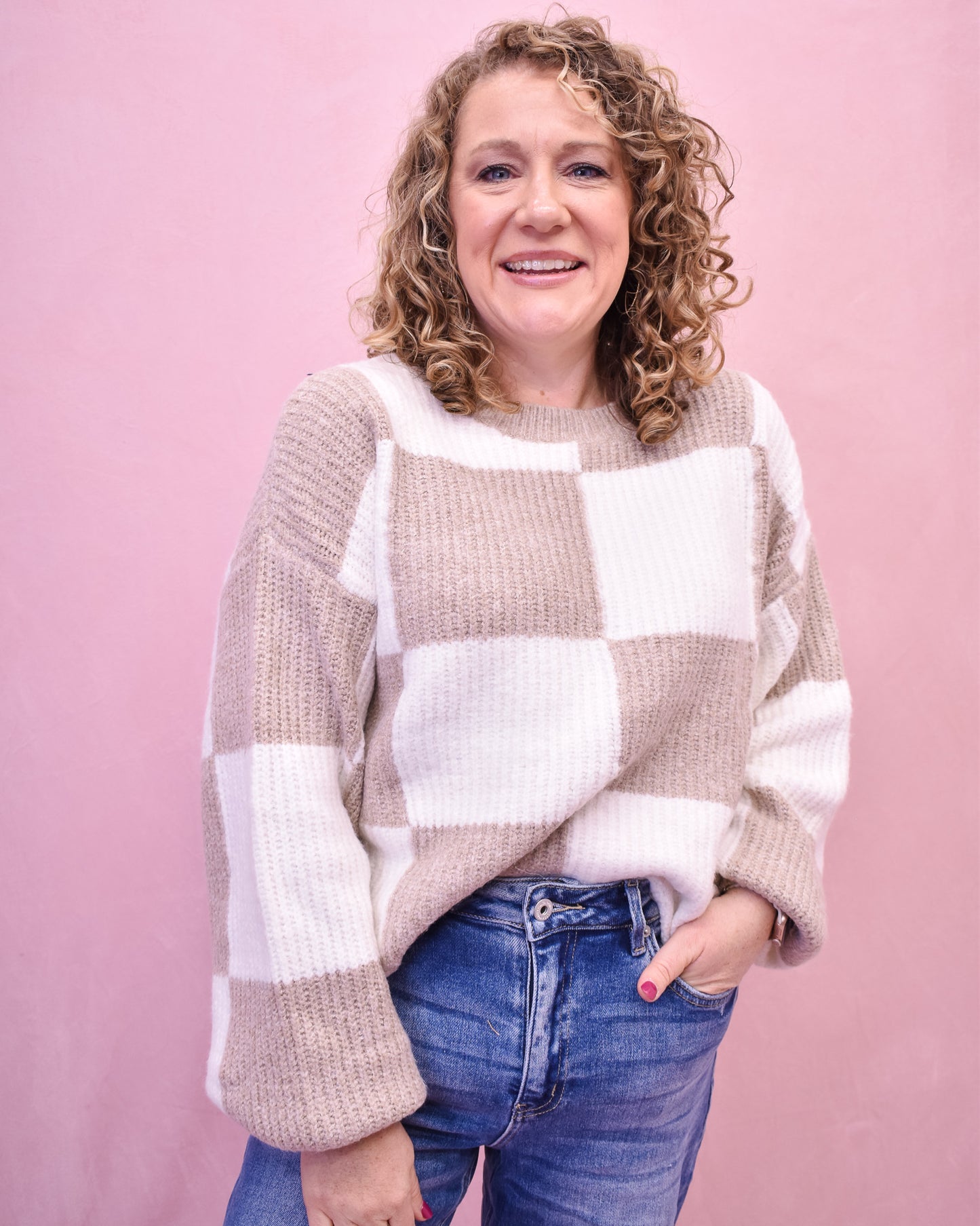 Woman wearing a checkered sweater and jeans against a pink background