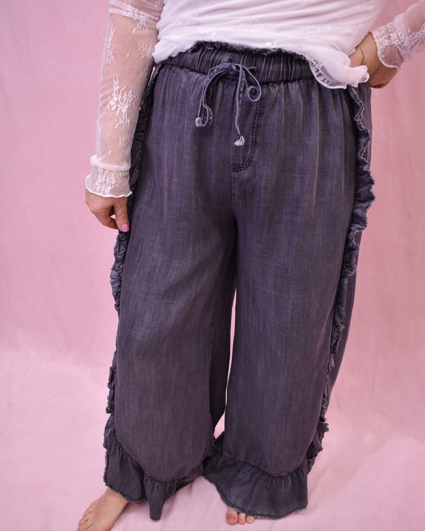Dark gray ruffled pants worn by a person on a pink background