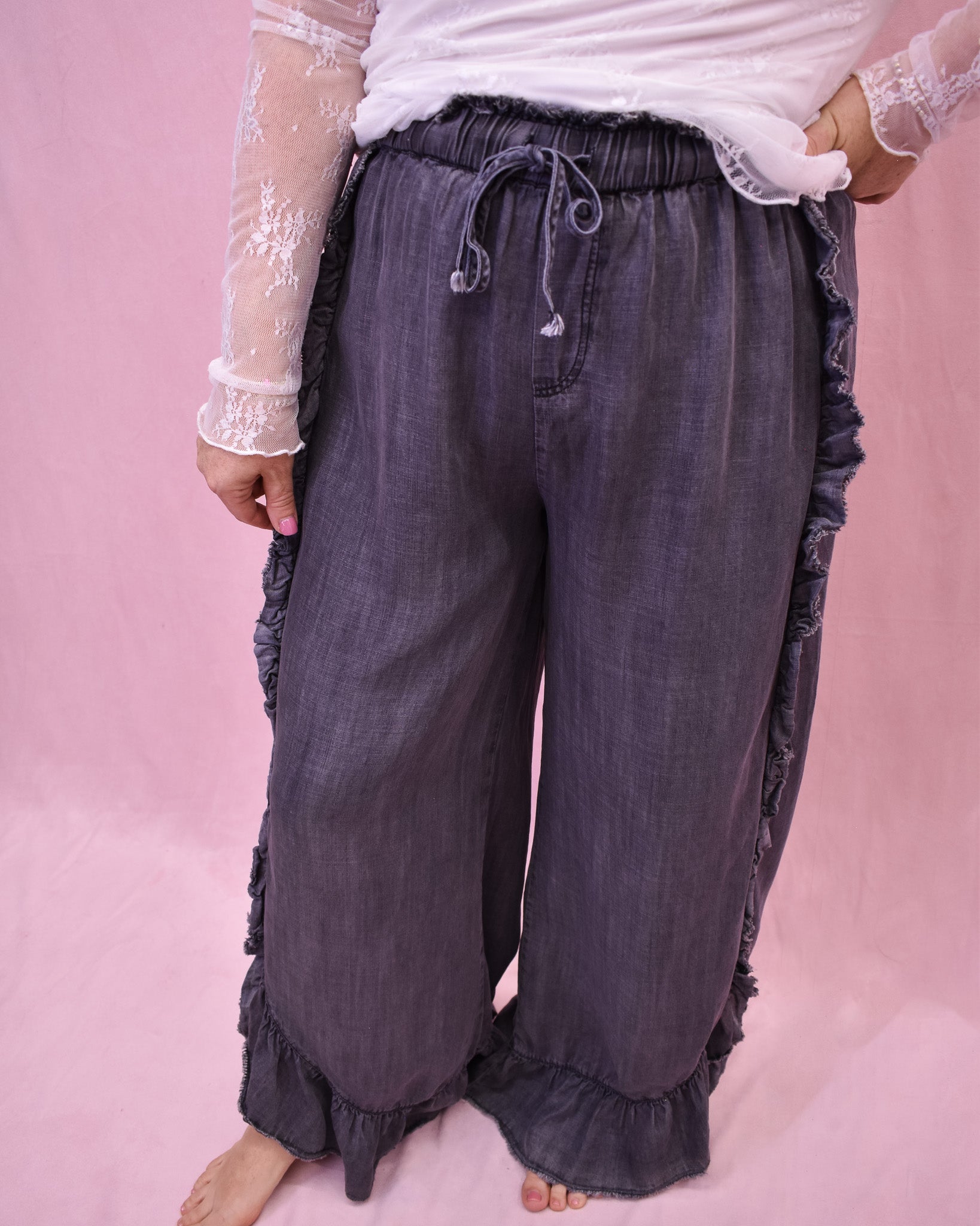Dark gray ruffled pants worn by a person on a pink background