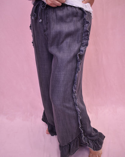 Dark denim jeans with ruffled details on a pink background