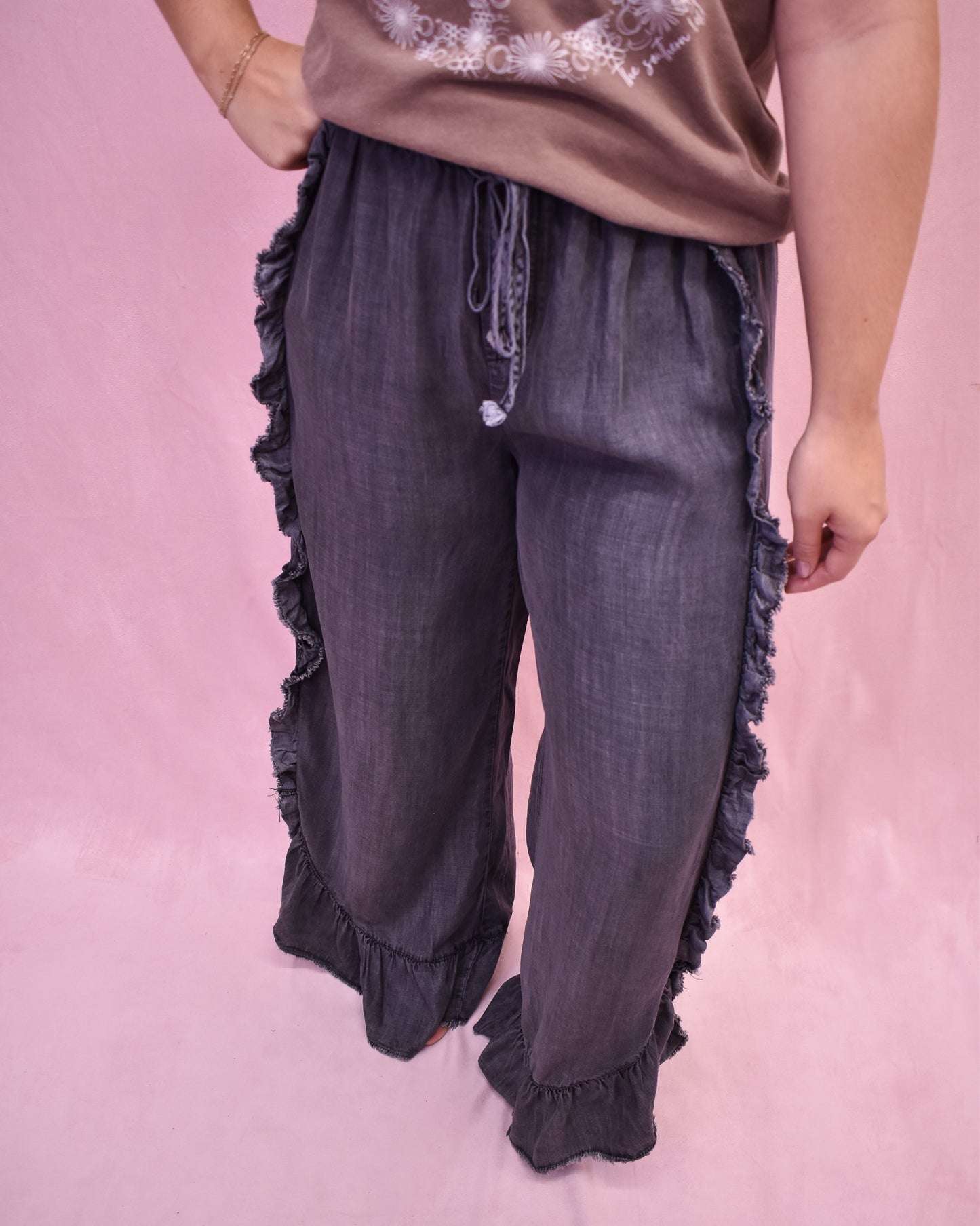 Dark gray ruffled pants worn by a person on a pink background