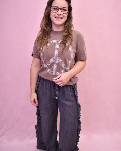 Person wearing a brown t-shirt with a peace symbol design and dark pants against a pink background