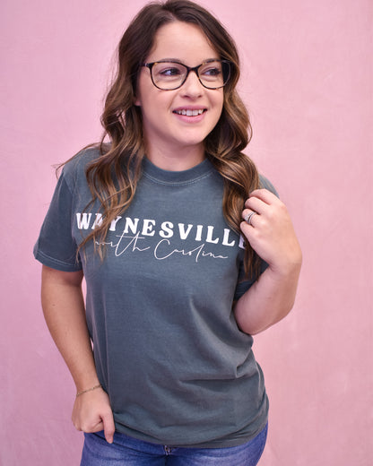 Woman wearing a blue t-shirt with 'Waynesville' text on a pink background
