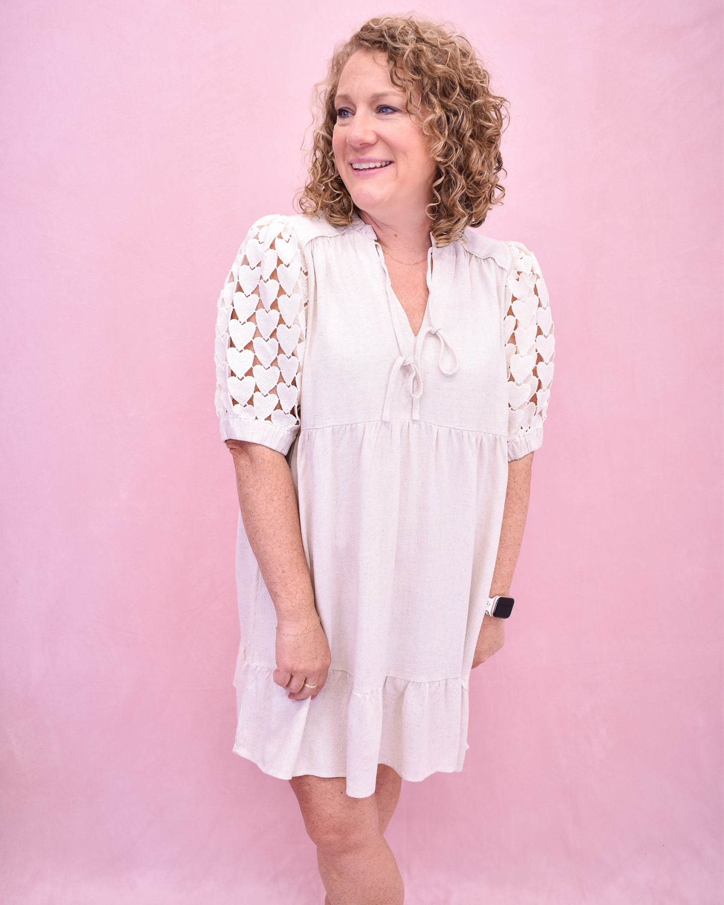 Woman wearing a white dress with lace sleeves against a pink background