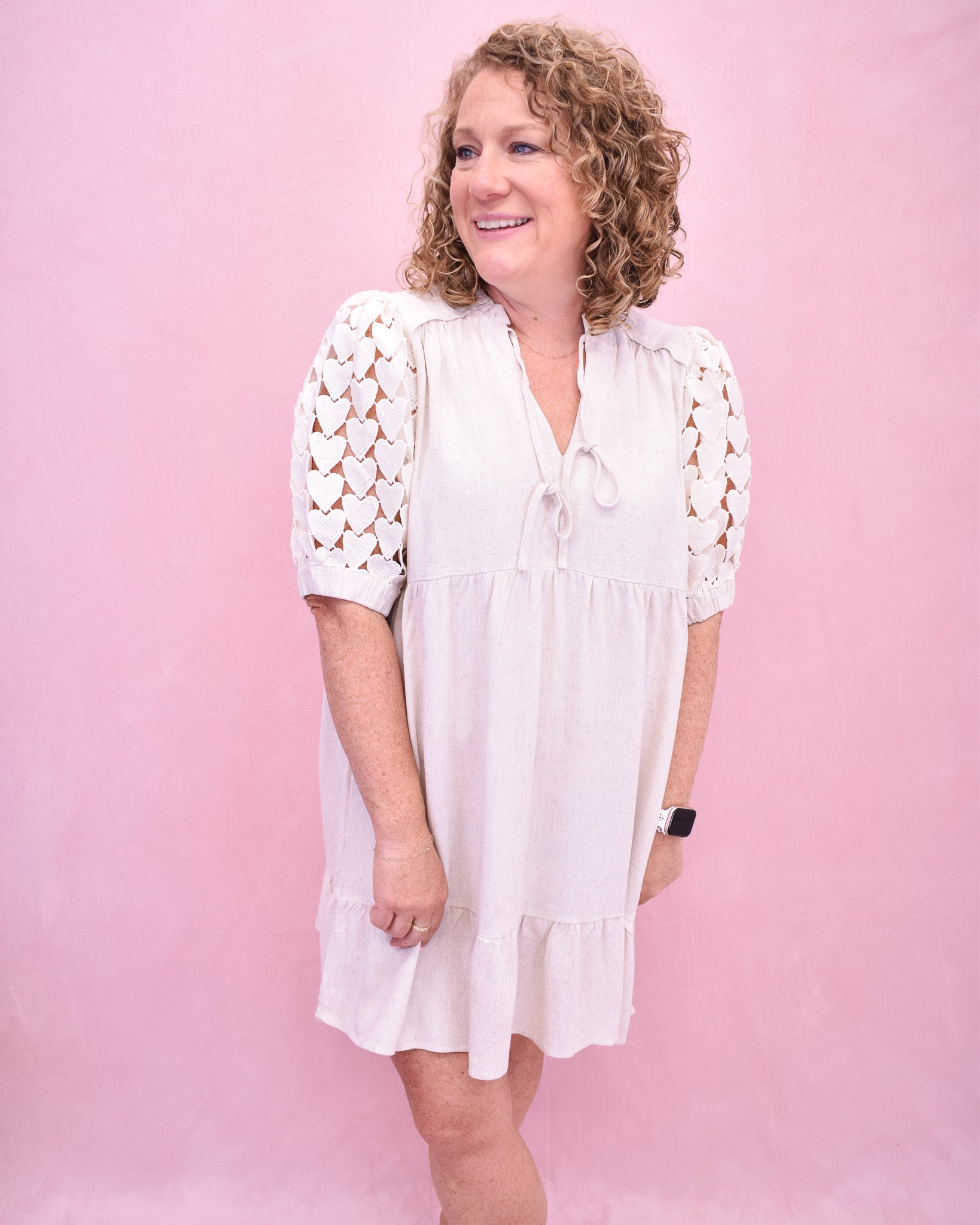 Woman wearing a white dress with lace sleeves against a pink background
