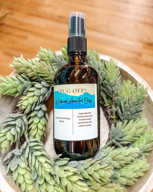 Bug spray bottle labeled 'Bug Off' surrounded by greenery on a wooden surface