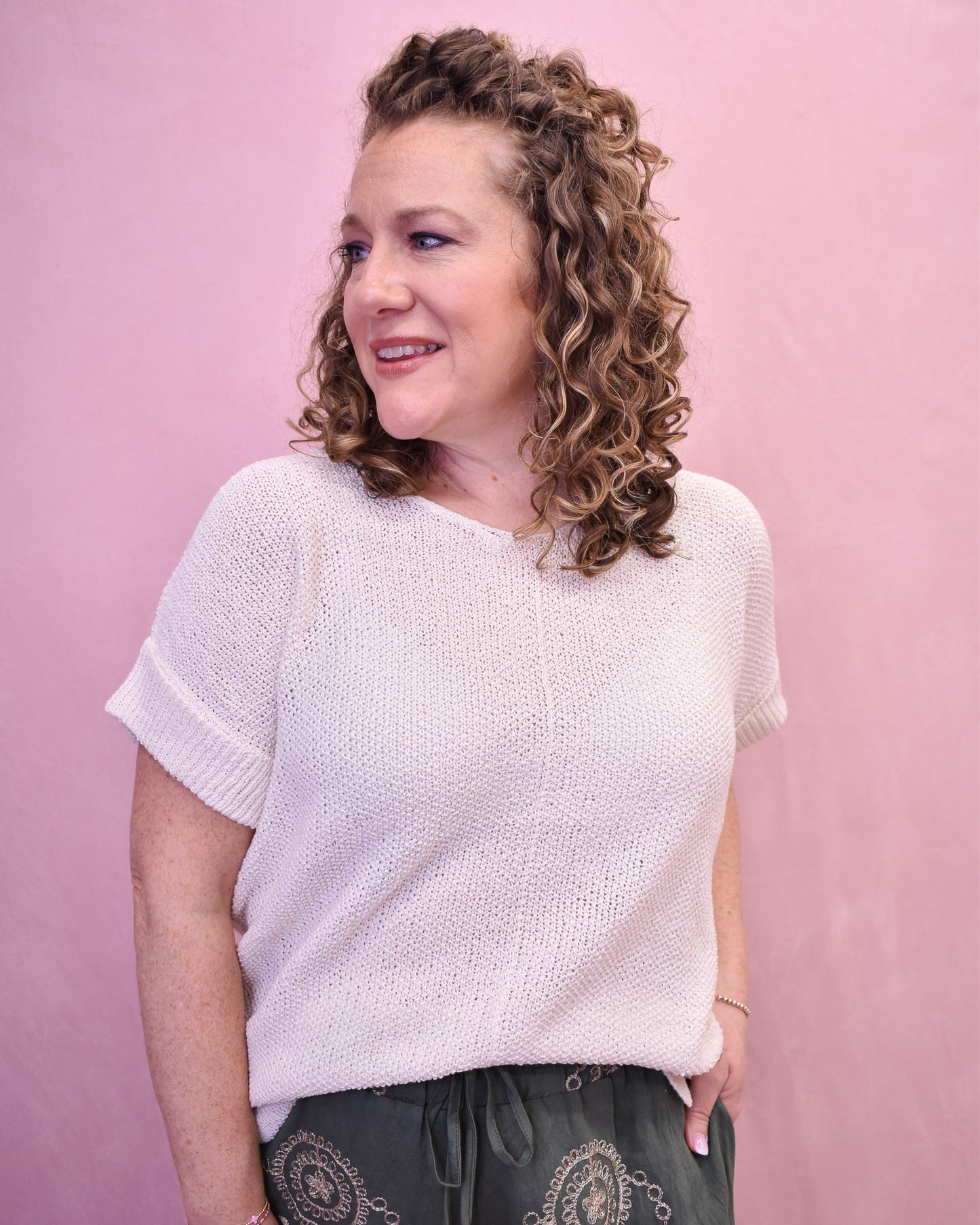 Woman wearing a white knit top against a pink background