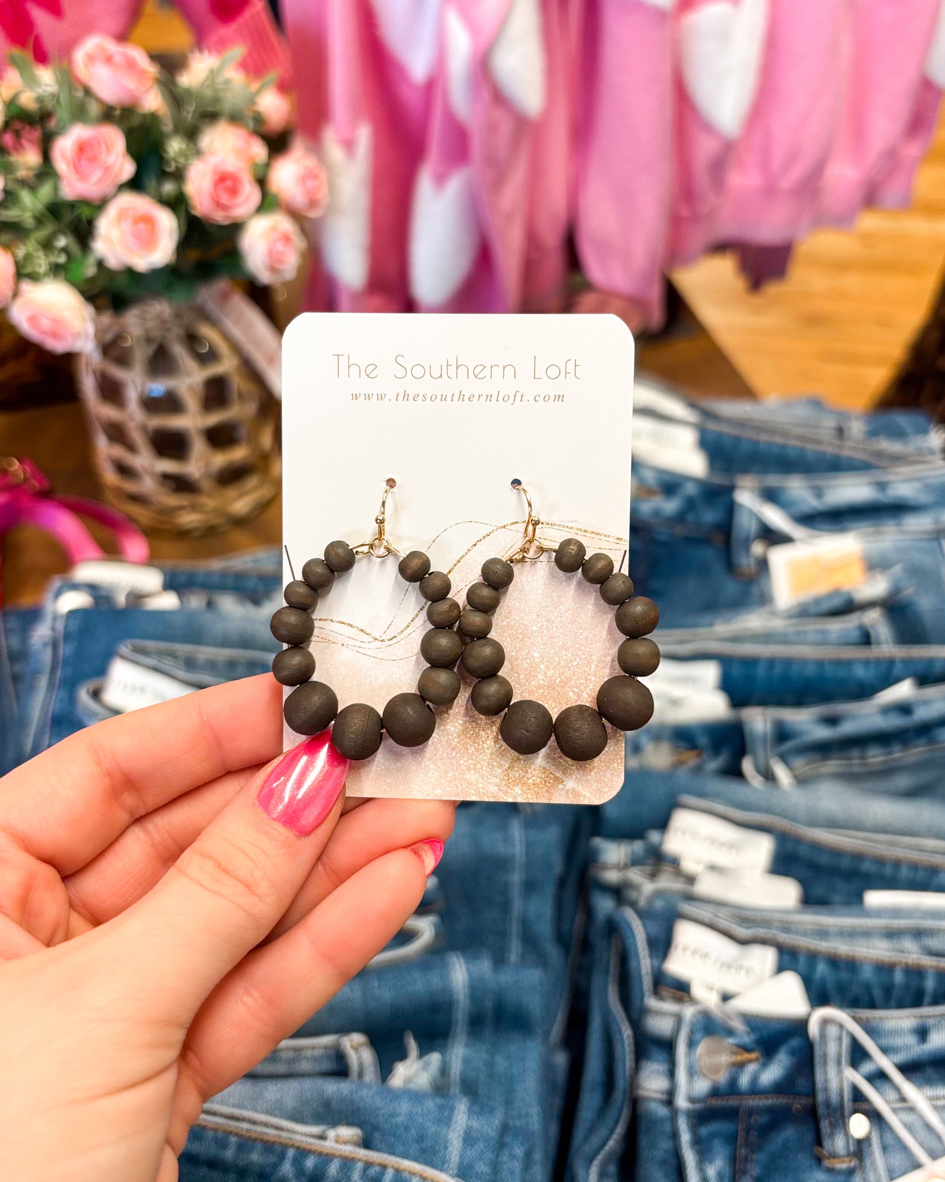 Hand holding a pair of beaded earrings on a card with denim and flowers in the background