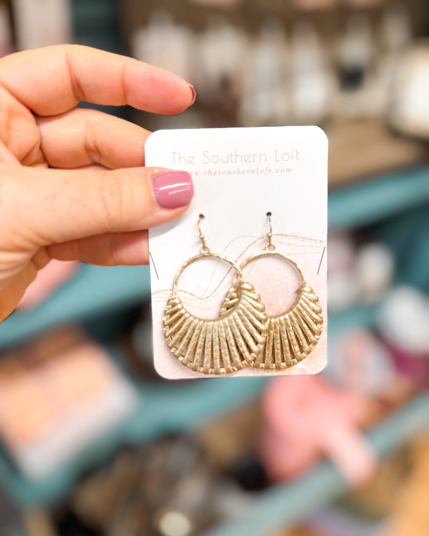 Gold hoop earrings on a card held by a hand with pink nail polish, blurred store background